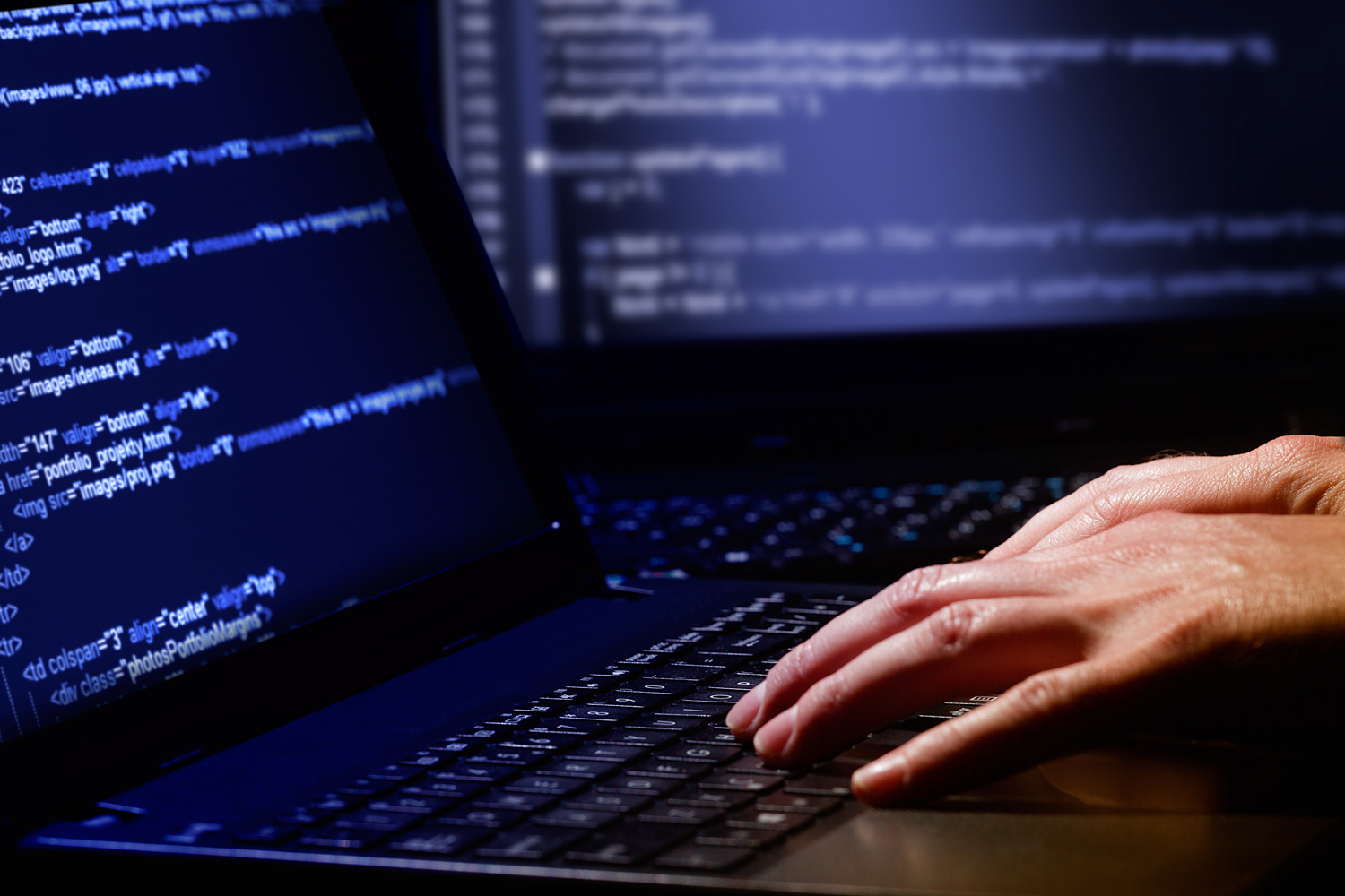 A pair of hands on a laptop keyboard with two displays.