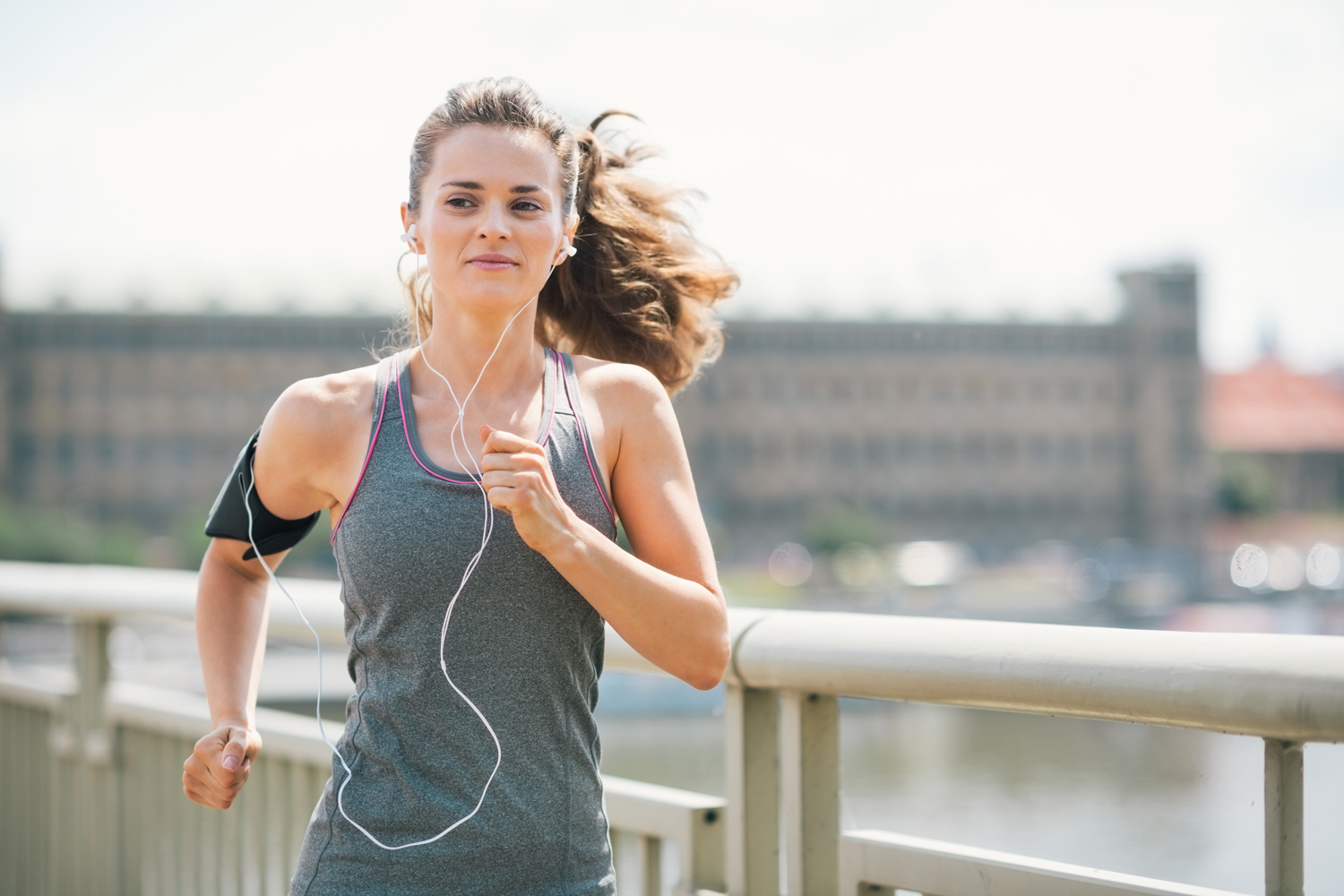 spotify songs popular in gym workouts woman jogging on waterfront with smartphone and earbuds