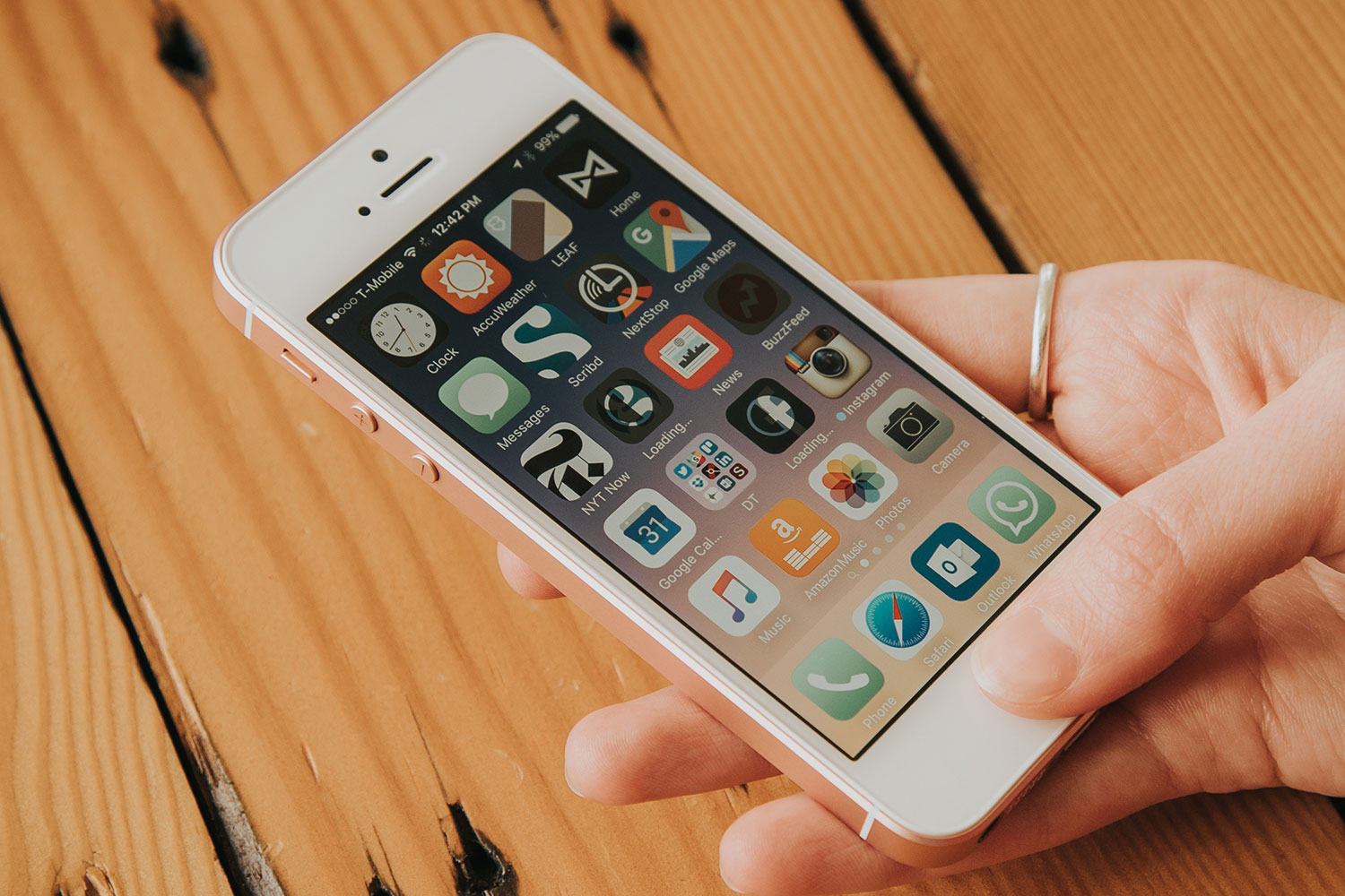 Someone holding an Apple iPhone SE next to a wooden surface.