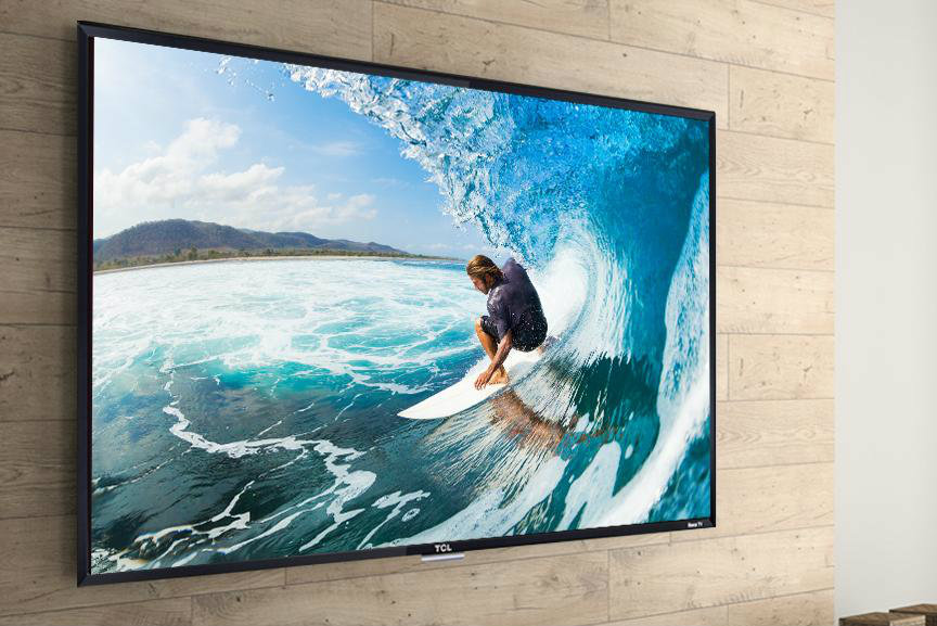 TCL 50 inch Roku Smart TV on a wood panel wall with surfer on the display.