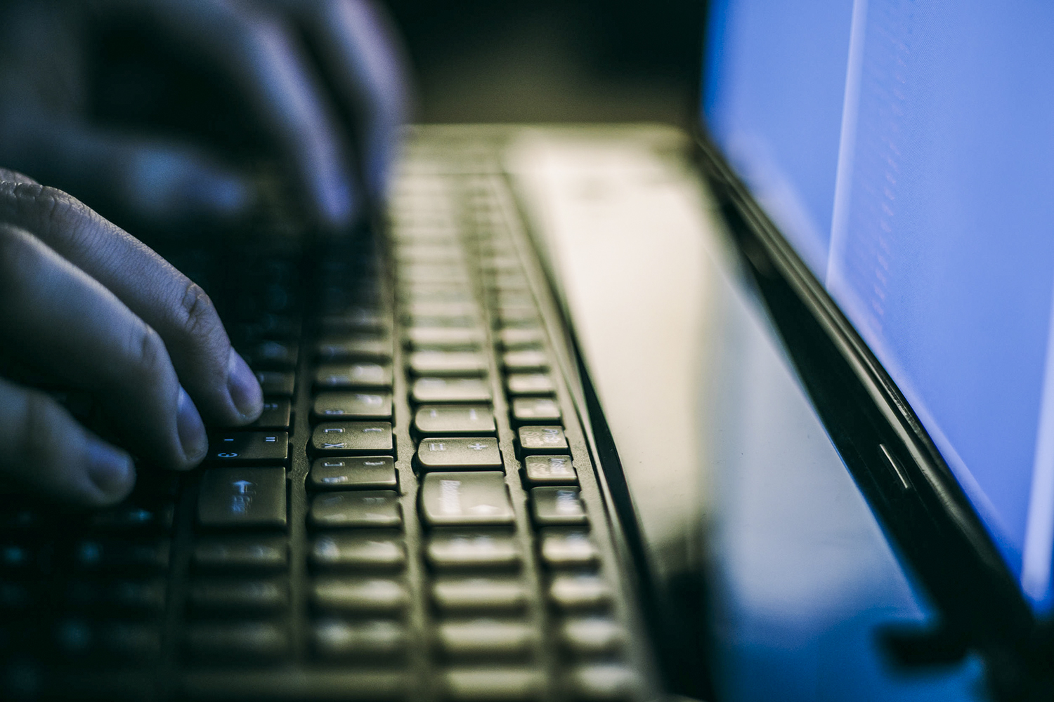 Close-up of hands on a laptop keyboard in a dark room.