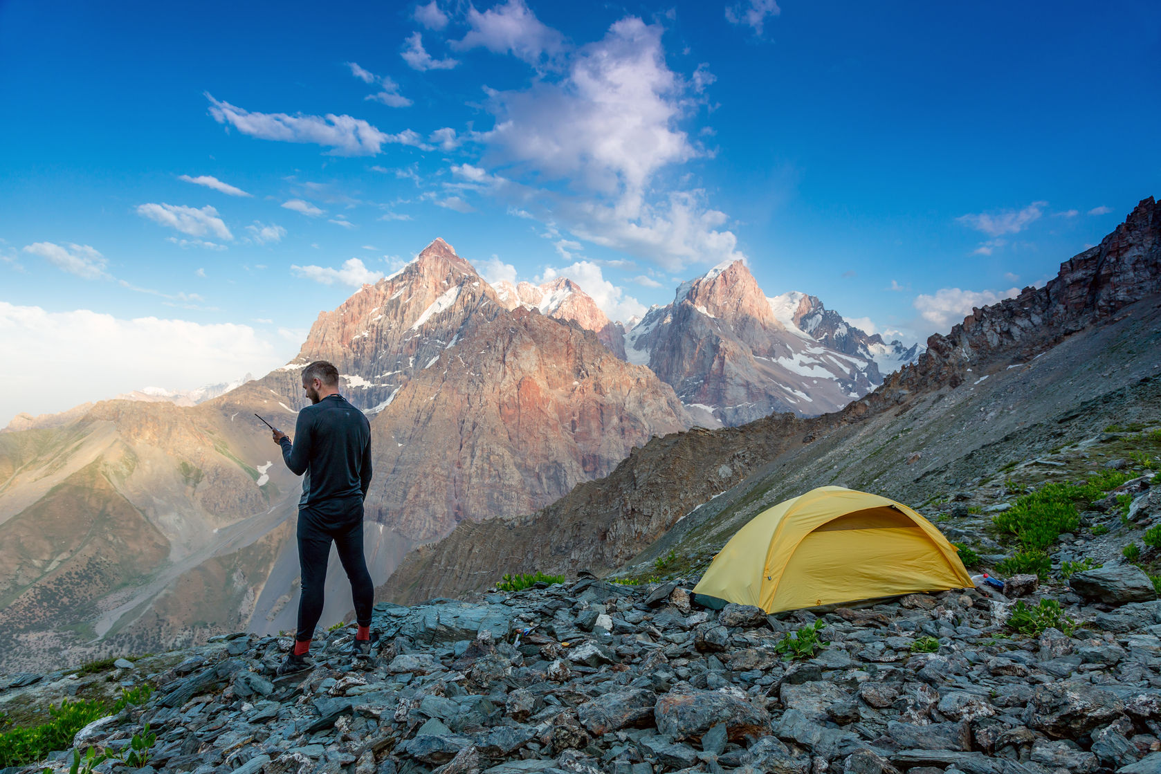 best satellite phones silhouette of man in wild mountain landscape walk along yellow camping tent holding phone