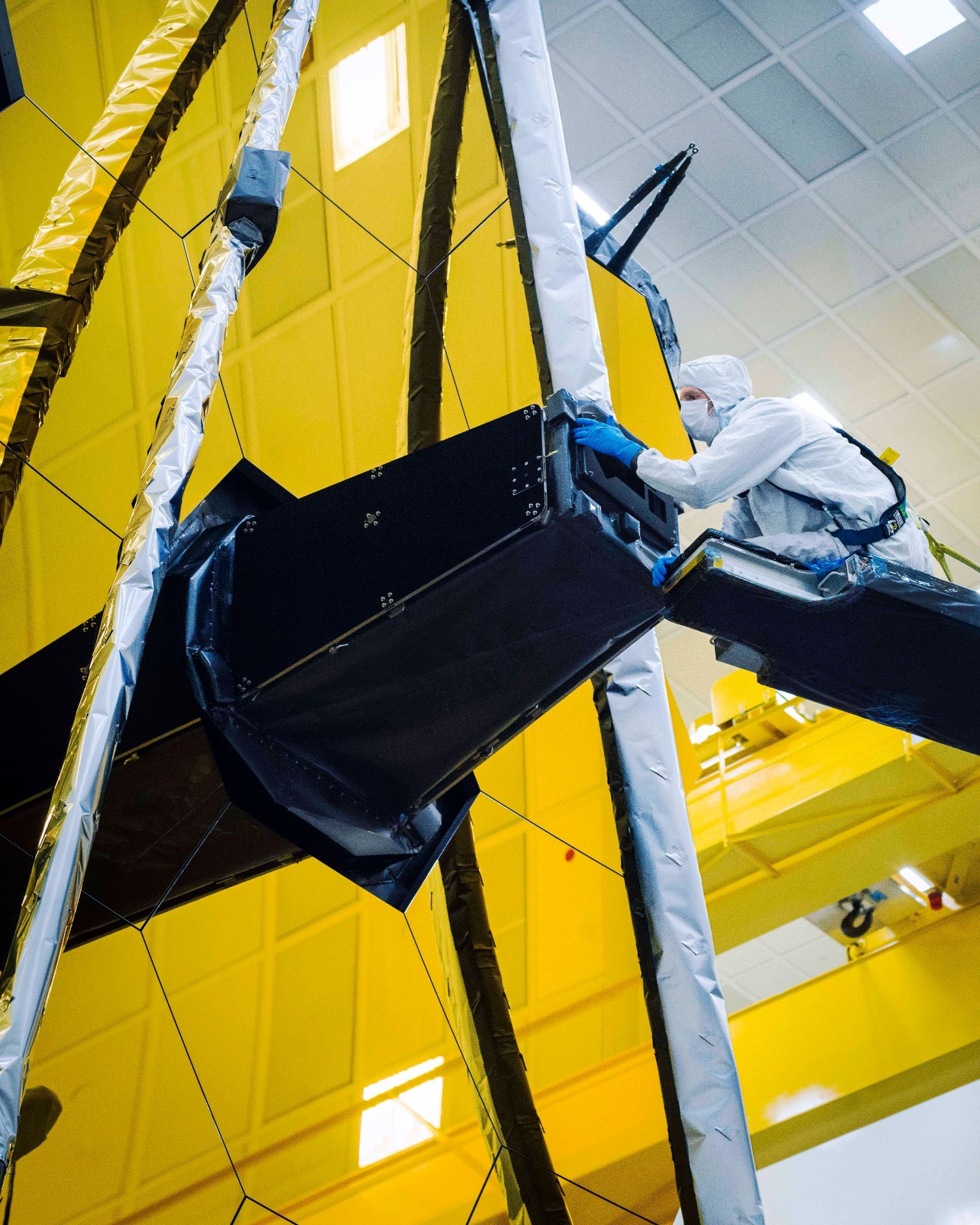 Ball Aerospace technician Larkin Carey can be seen carefully removing Webb’s "lens cap" from the Aft Optics Subsystem which has kept the observatory’s sensitive instruments clean, contaminant-free, and protected from stray light throughout the integration and test process.