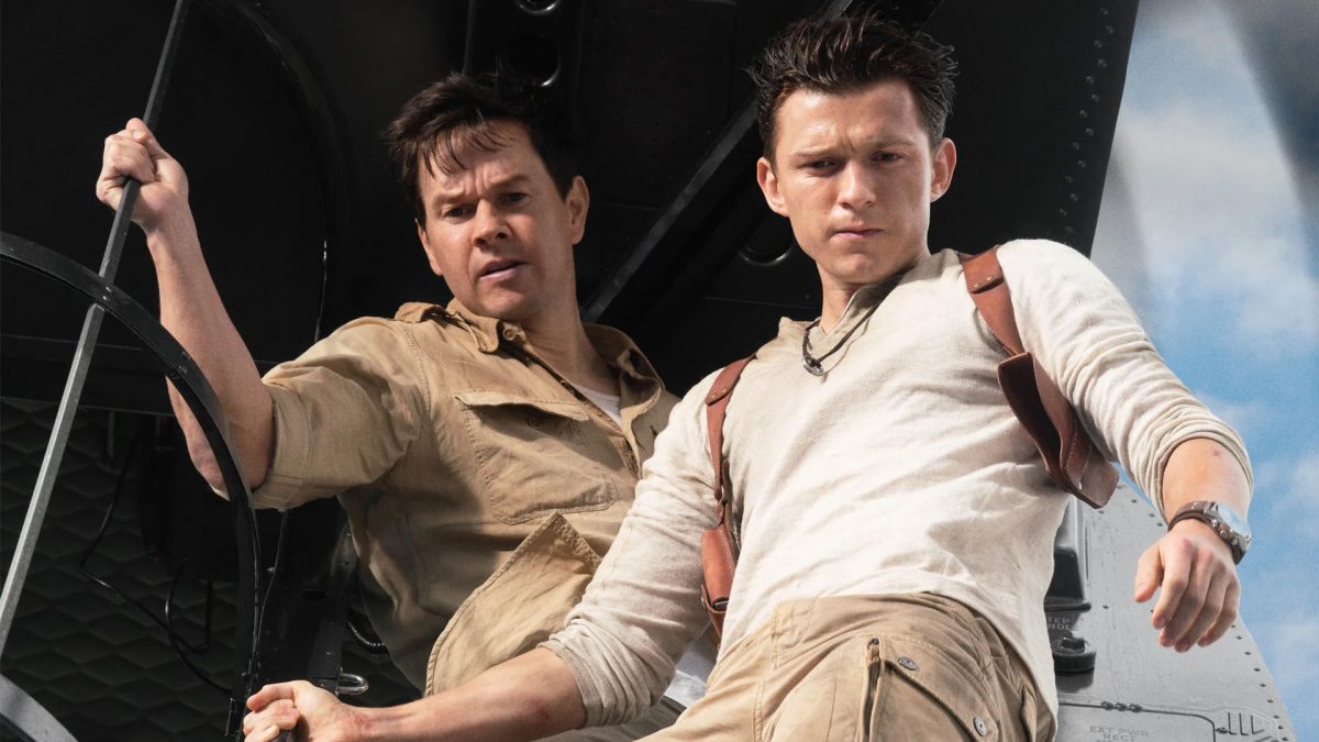 Tom Holland and Mark Wahlberg stand on the edge of a plane and stare down.