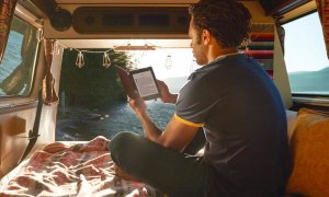 A young man reads a book in his car on the Amazon Kindle Paperwhite.