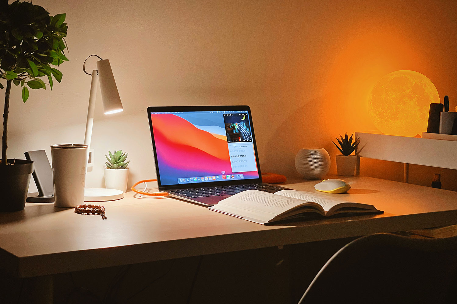 A MacBook Air on a desk with an open book in front of it.