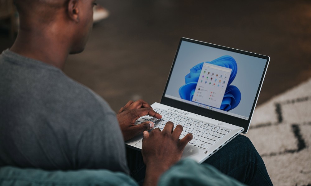 A man sits, using a laptop running the Windows 11 operating system.