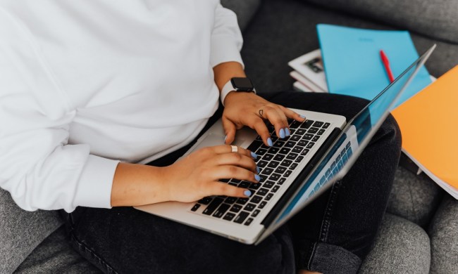 A close-up of someone's hands as the person sits on a couch and types on a laptop.