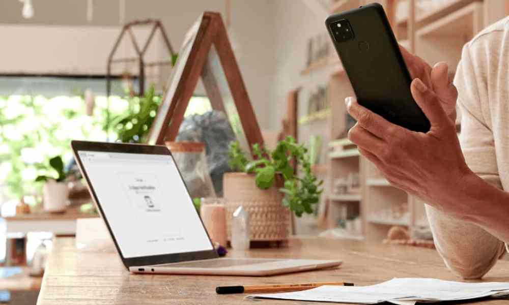 Person using smartphone at home office desk beside open Chromebook.