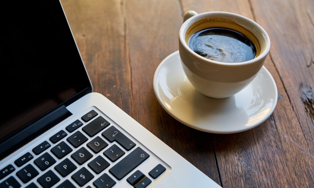 MacBook next to a coffee cup on a table.