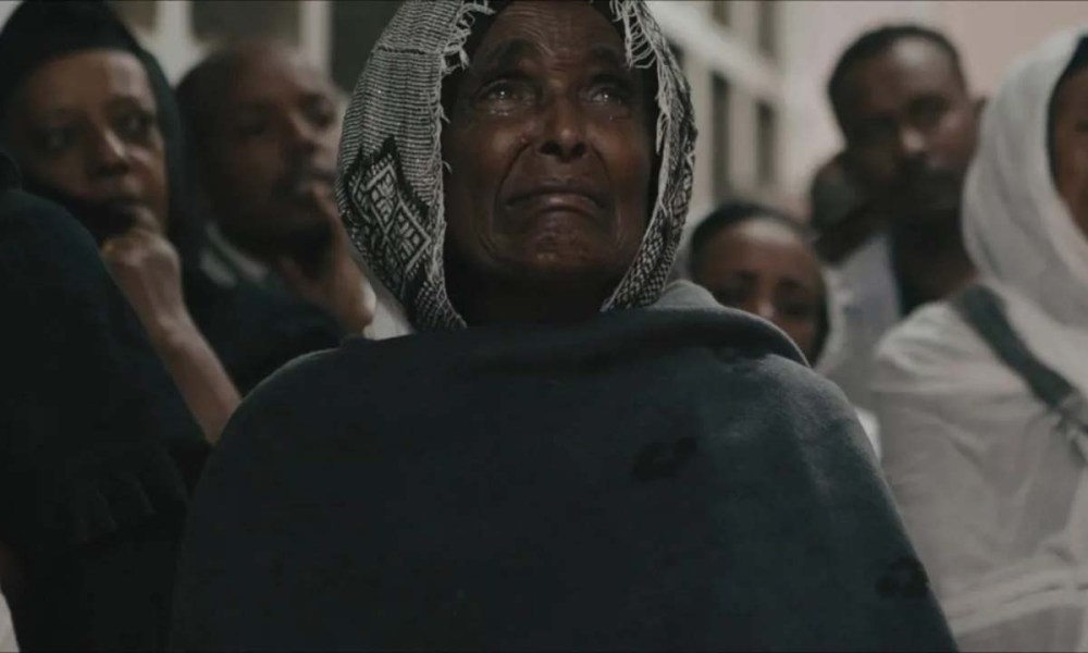 An older woman with a headscarf looks up, looking distraught in a scene from Flight/Risk on Amazon Prime.