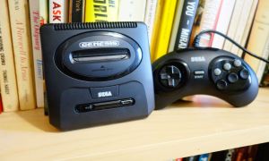 A Sega Genesis Mini 2 and its controller sit on a bookshelf.