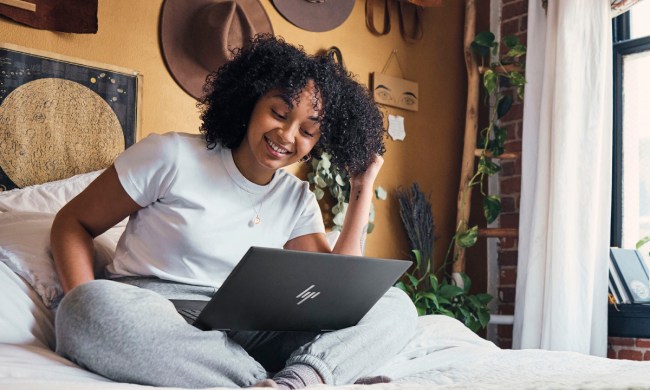 A person using a HP ENVY x360 2-in-1 15.6-inch Touch-Screen Laptop sitting on a bed.