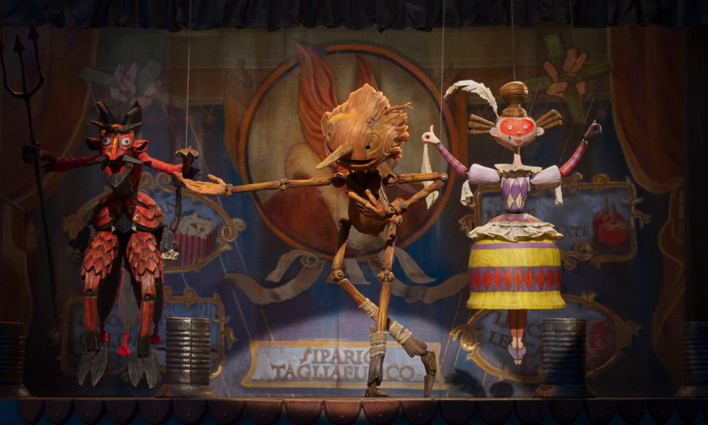 Pinocchio bows while performing on stage with several marionettes.