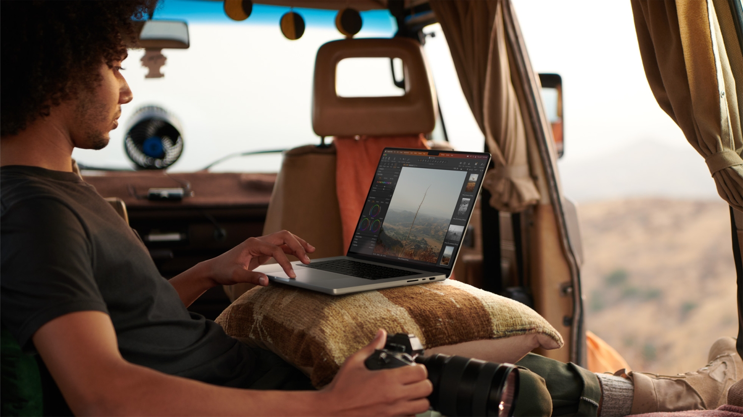 A person sitting in a vehicle using a MacBook Pro on their lap.