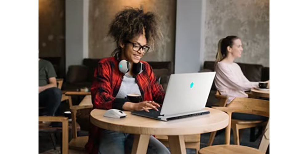 A woman using the Dell G16 gaming laptop in a coffee shop.