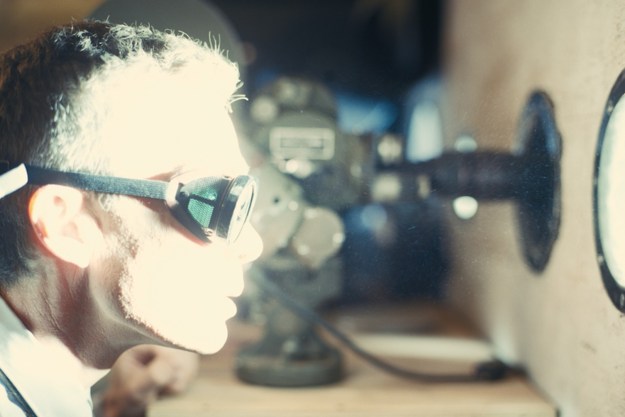 Cillian Murphy stares through a small window at an atomic blast, his face illuminated by light.