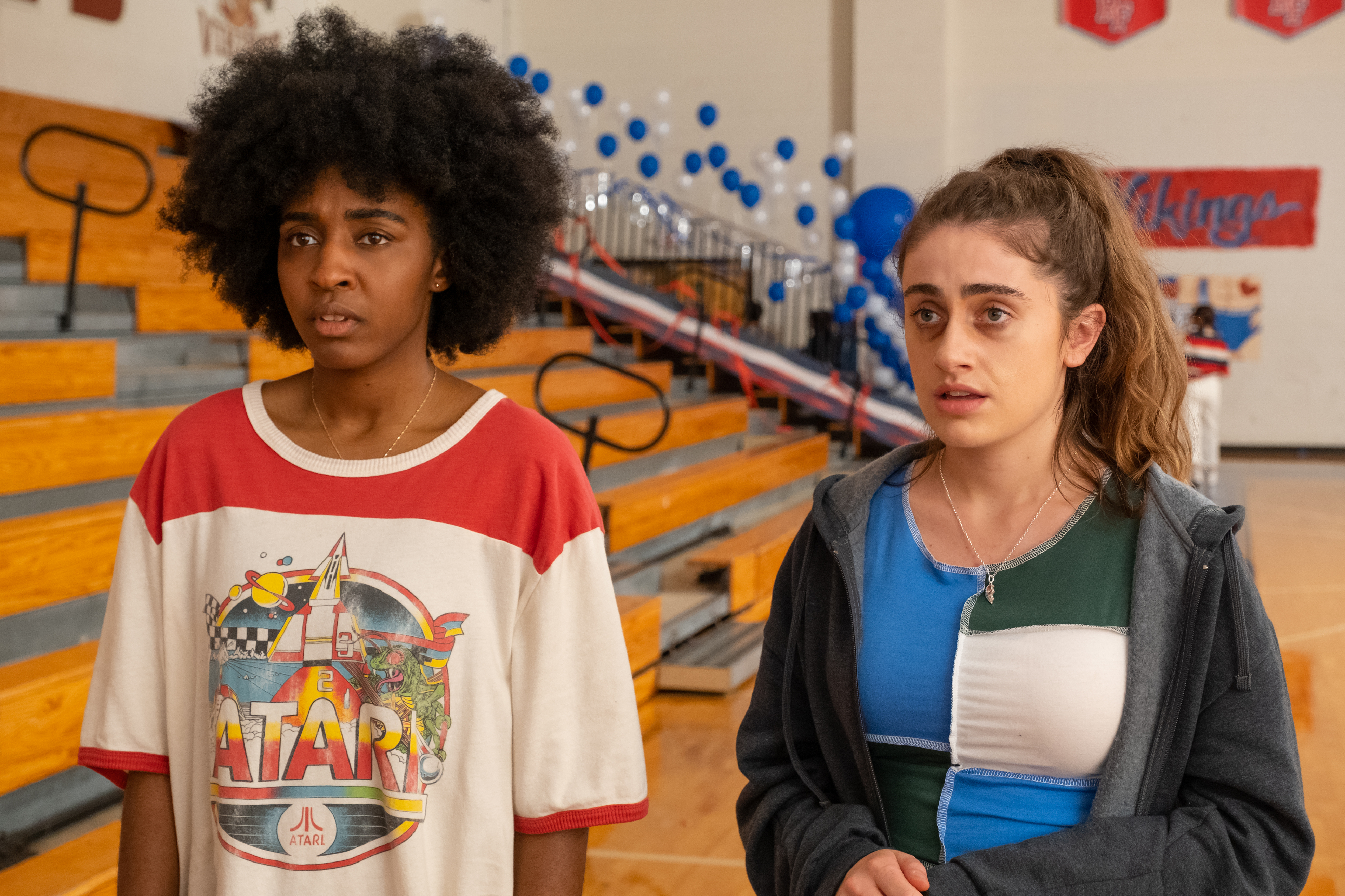 Ayo Edebiri and Rachel Sennott stand near a set of gym bleachers in Bottoms.