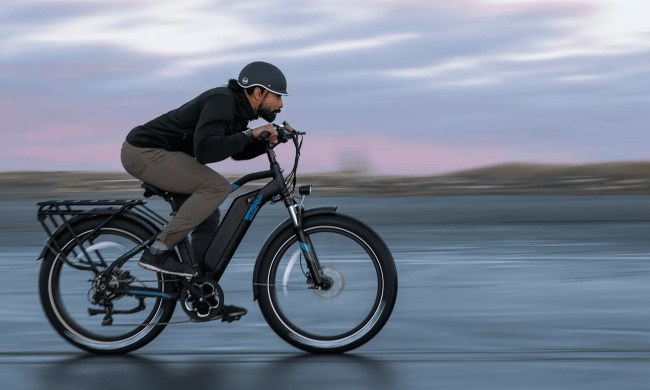 A male rider crouched down riding an Ariel eBikes Kepler fat tire e-bike on hard-packed beach sand.