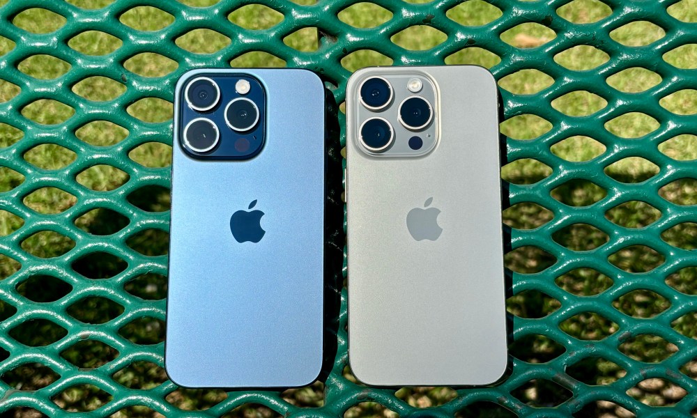 Blue Titanium (left) and Natural Titanium iPhone 15 Pros on a green park bench.