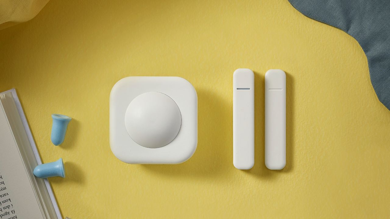 The upcoming Ikea motion sensor and door sensor on a yellow desktop.