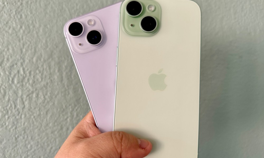 Purple iPhone 14 (left) and a green iPhone 15 in hand.