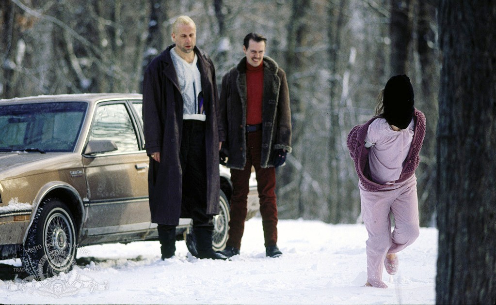 Two men watch a woman run in the snow in Fargo.