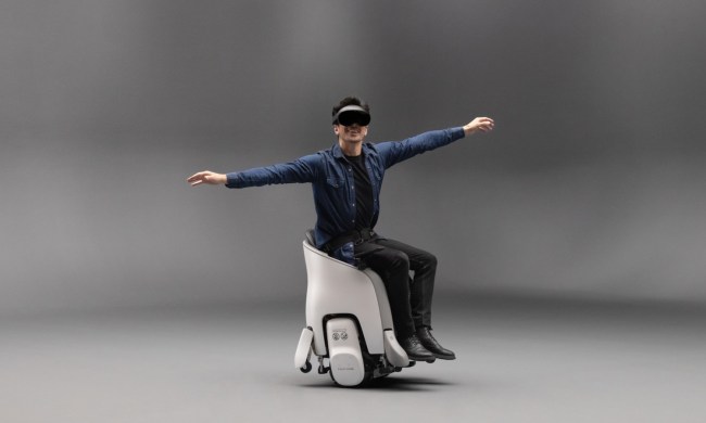 A person sitting in a Honda Uni-One wearing a VR headset with their arms outstretched in pretend-flying position.