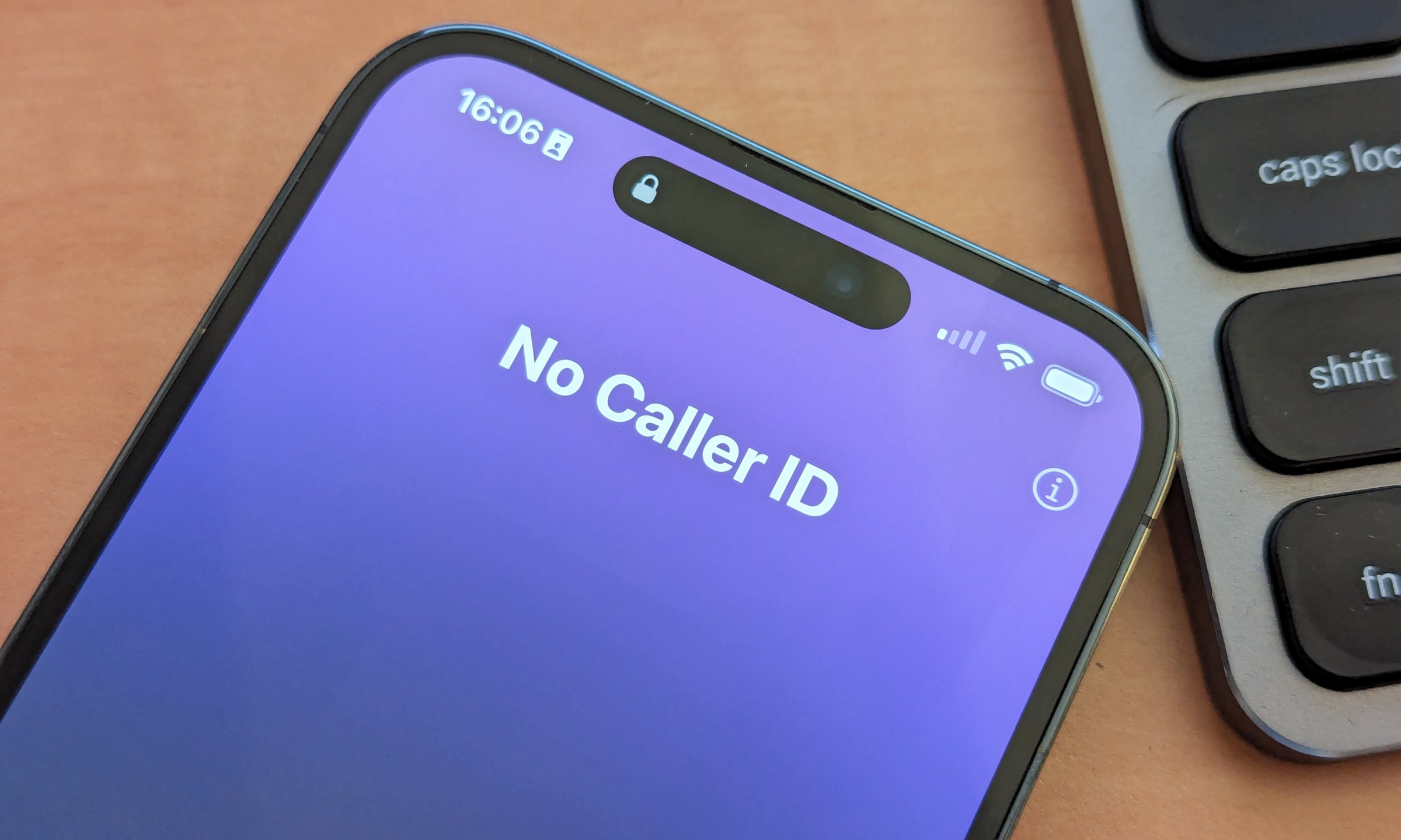 iPhone 14 Pro Max laying on a desk beside a keyboard with an incoming call showing No Caller ID.