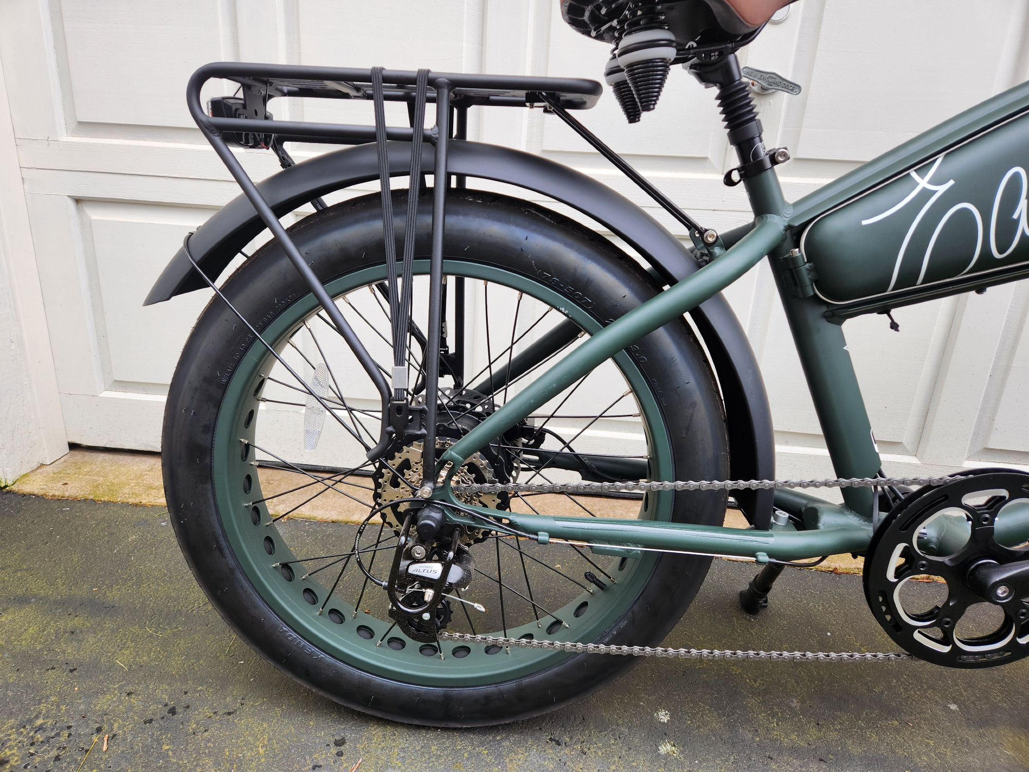 Right profile shot of a MOD Easy rear wheel with hub motor, gearing, and rear rack parked in front of a white garage door.