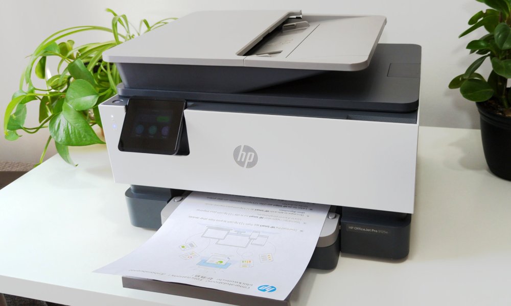 The HP OfficeJet Pro 9125e rests on a white stand surrounded by plants.