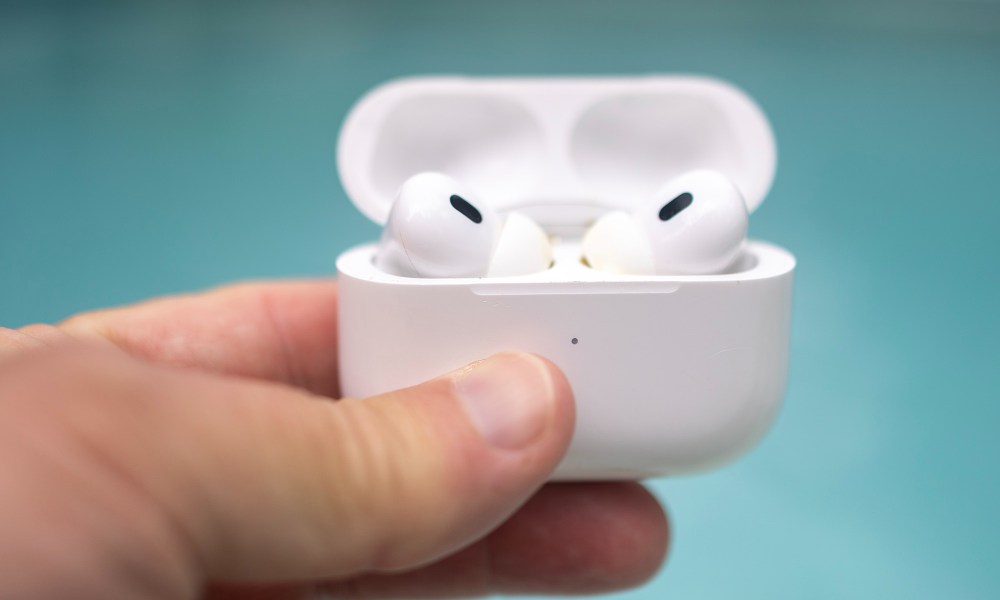 A pair of Apple AirPods Pro in an open case with a swimming pool in the background.