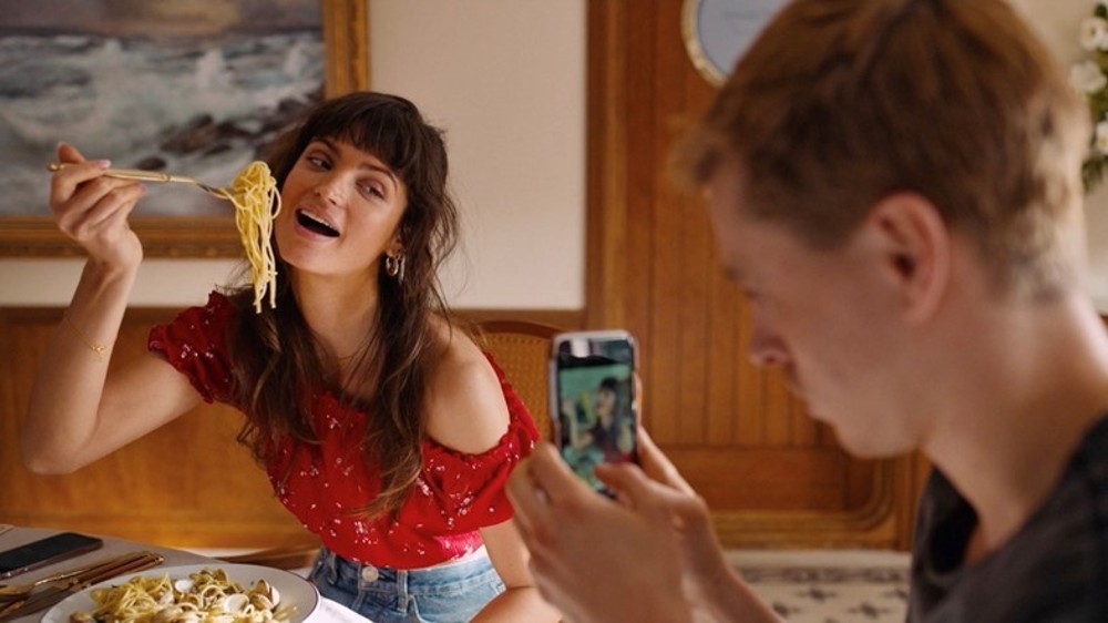 A man films a woman eating pasta in Triangle of Sadness.