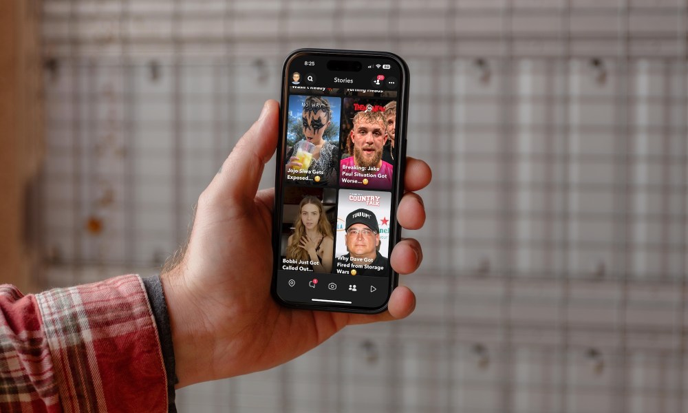 A guy holding an iPhone with Snapchat on in dark mode.