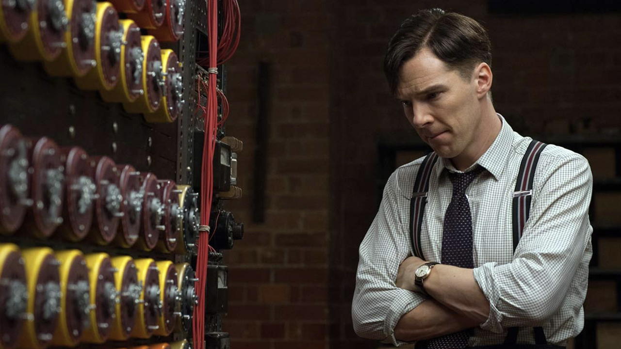 Benedict Cumberbatch looking at a series of electronic devices with his arms folded in a scene from The Imitation Game.