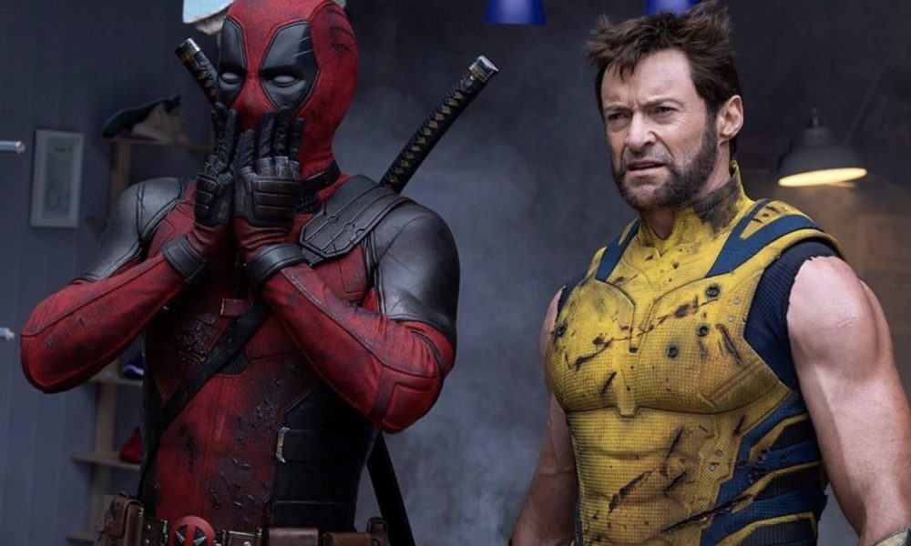 Deadpool puts his hands over his mouth while Wolverine stands next to him.