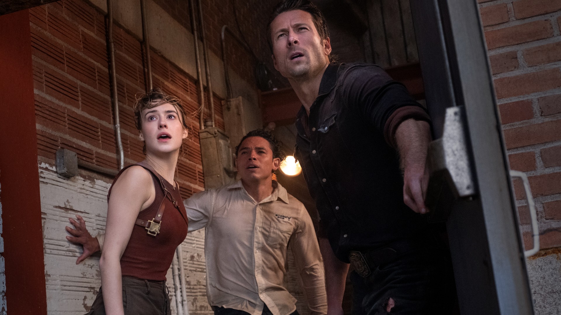 Daisy Edgar-Jones, Anthony Ramos, and Glen Powell stare offscreen at a tornado, probably, in a still from the movie Twisters.