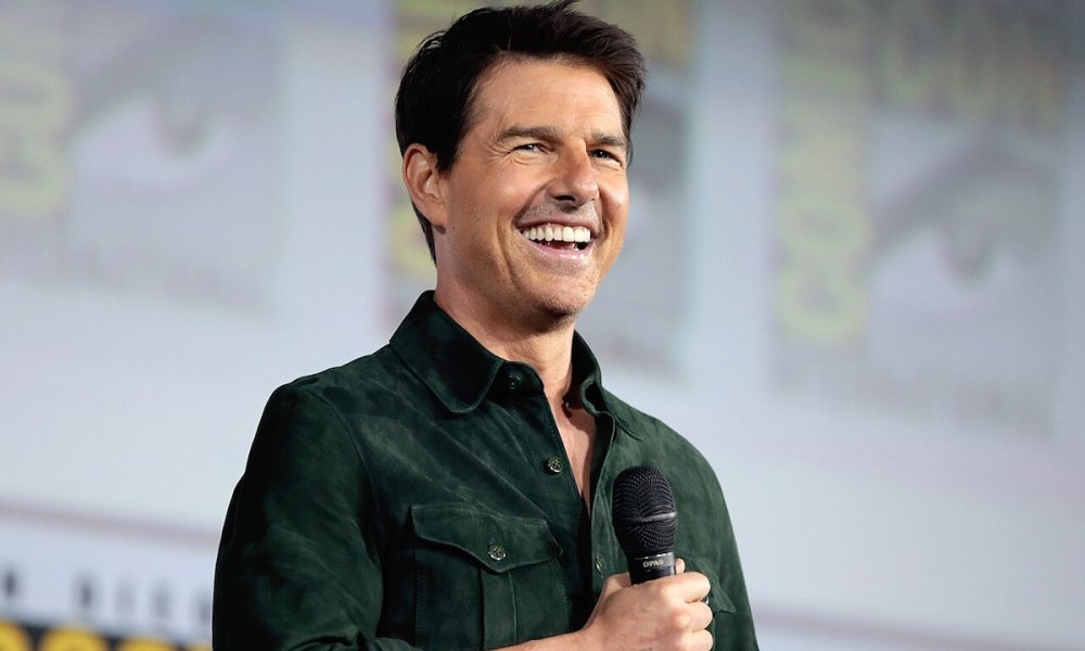 Tom Cruise smiles while holding a microphone.