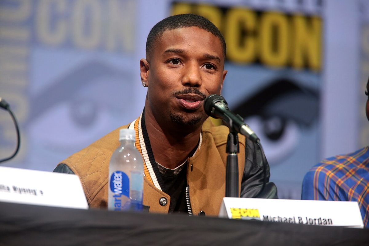 Michael B. Jordan sits at a podium and talks.