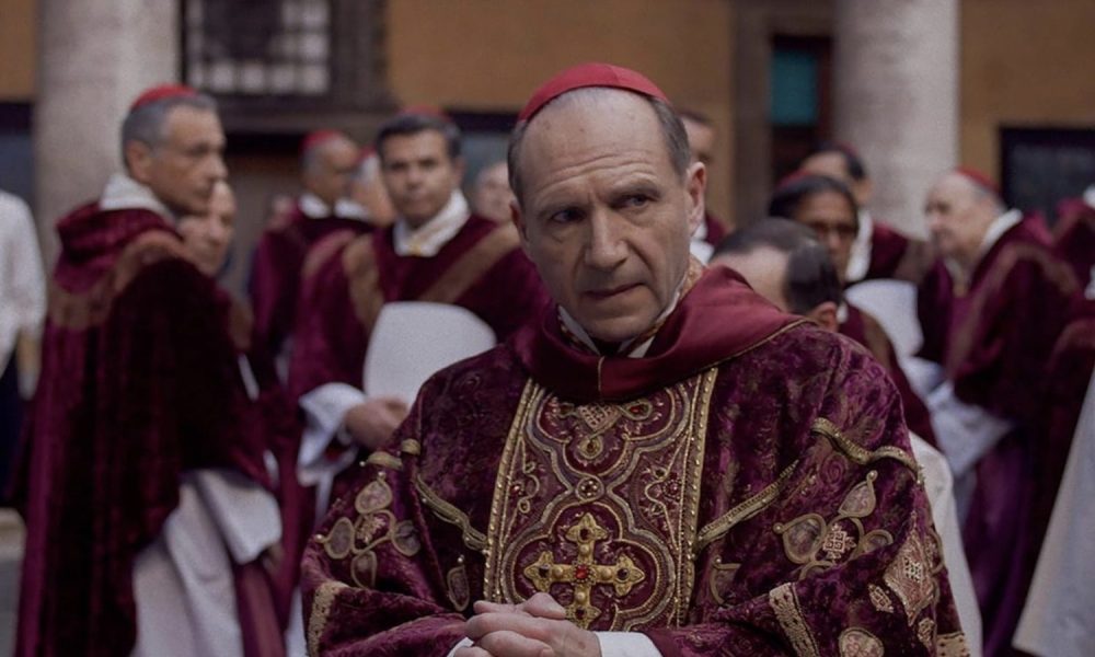 Ralph Fiennes dressed as a pope looks to his left.