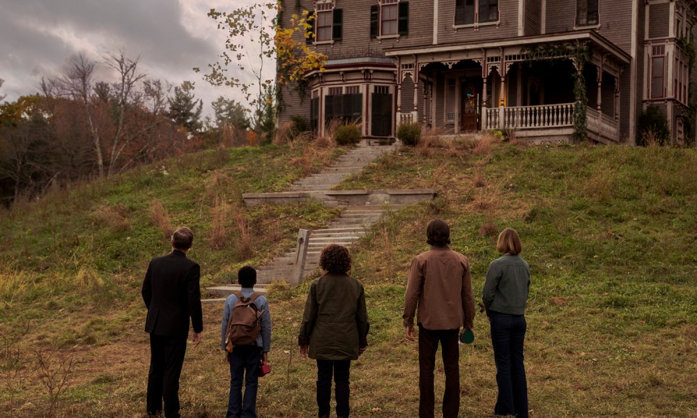 Five people stand at the bottom of the hill and stare at a house.