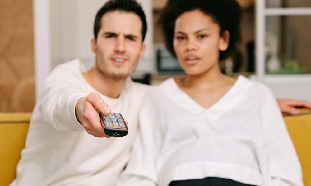 A frustrated-looking couple holds a TV remote.