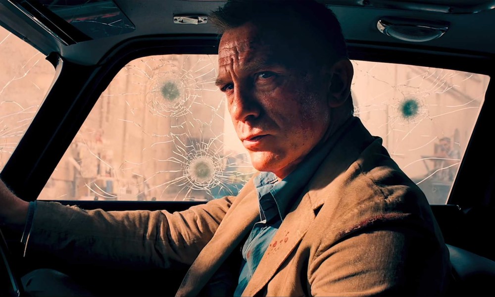 Daniel Craig as James Bond in a car peppered with bullet holes in No Time to Die.