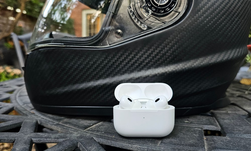 Apple AirPods Pro 2 sitting in front of a motorcycle helmet.