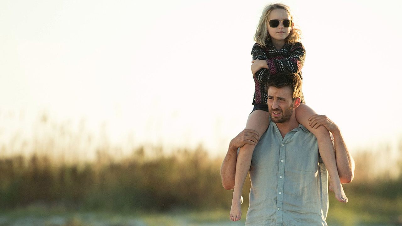 Chris Evans outdoors in a field with a young girl wearing sunglasses over his shoulders in Gifted.